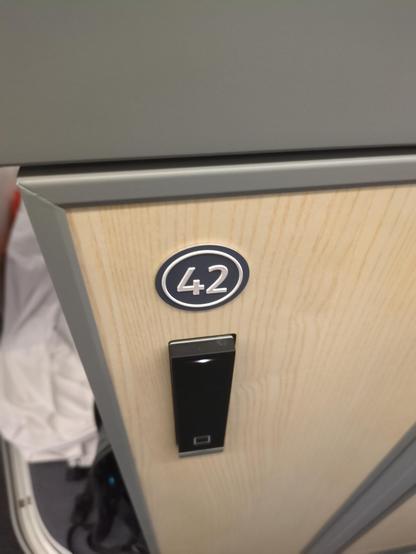 Close-up view of the outer wall of an ÖBB Nightjet Mini Cabin

On it, a small circular label is showing the cabin number 42. Below is the key card reader to open the door and the luggage/shoe lockers.