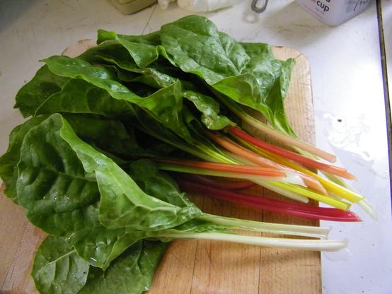 Leafy plant stalks. The leaves are green, while the stems are pink, yellow, pale orange, and white. The leaves are on a cutting board on a kitchen counter.