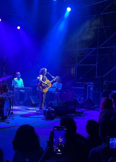 Ani DiFranco bellissima come sempre sul palco con la chitarra. Dietro di lei i musicisti. Luci blu. In basso altri spettatori