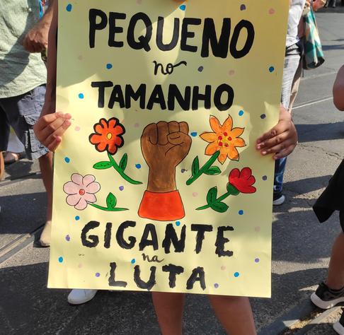 Cartaz com um desenho de um punho fechado, de cor castanha, rodeado de flores. O título do cartaz é "Pequeno no tamanho, gigante na luta"