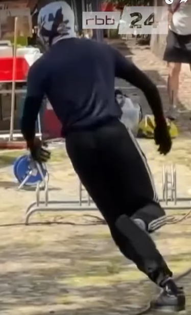 Der Screenshot zeigt eine Person in dunkler Kleidung mit weiß-schwarzer Sturmhaube.