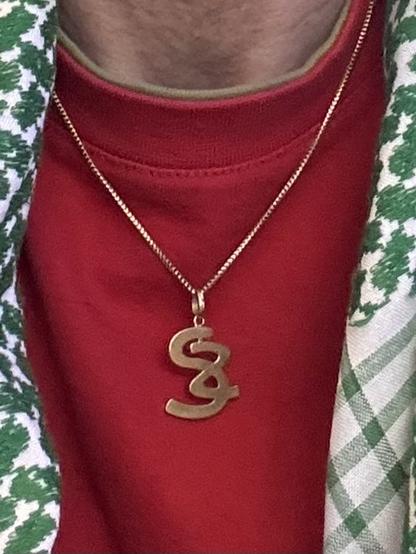 Gold chain on a red shirt with pendant showing S & Z intertwined.