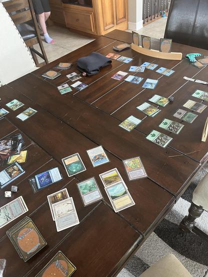 A photo of our kitchen table with Magic: The Gathering cards laid out after about 7 rounds of play.