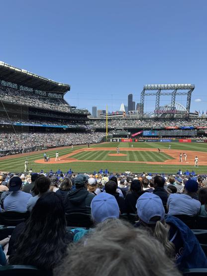 The image depicts a baseball game in progress at Safeco Field on a sunny day. The field is well-maintained with a green outfield and a dirt infield, and the players are dressed in traditional baseball uniforms. The batter is at the plate, ready to swing, while the pitcher is in the middle of his windup. The crowd is visible in the foreground, with many spectators wearing baseball caps and team colors, indicating their support for the home team. The stands are filled with fans, and the atmosphere appears lively and energetic. In the background, the city skyline is visible, with tall buildings and a clear blue sky. The stadium features a prominent scoreboard and large light towers, typical of professional baseball venues. The overall scene captures the excitement and communal spirit of a live baseball game.

Provided by @altbot, generated privately and locally using Ovis2-8B