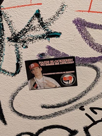 Aufkleber auf einer beschmierten Toilettenwand, auf dem ein Bild von Money Boy drauf ist mit dem Satz "Nazis blockieren wo immer die appearen".