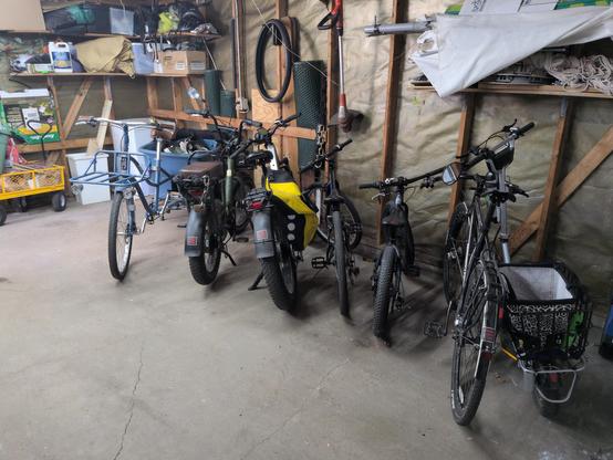A Madsen bucket bike, two ebikes, a single-speed bike and two kids' bikes lined up in a slightly less dingy than earlier today garage