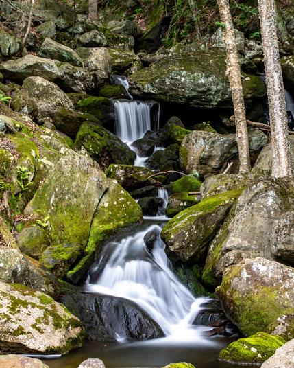 A long exposure of narrow-ish waterfall over large boulder covered in mosses