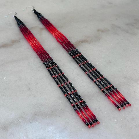 A pair of long beaded dangles in shades of red, grey, and black on a white marble background.