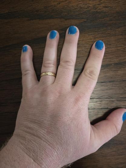 Photograph of a white person's left hand with a golden ring on the ring finger and their fingernails painted in a bright blue.