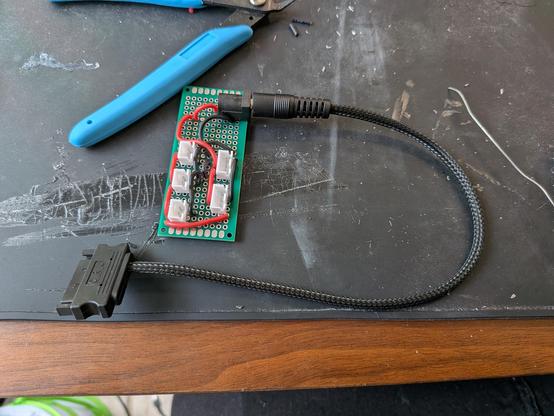 A proto circuit board with a barrel jack and a few jst sockets soldered to it. A SATA to barrel jack cable is plugged into it.