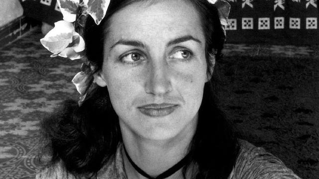 Retrato en blanco y negro de Françoise Gilot, con flores en el cabello y un fondo con patrones decorativos.