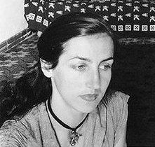 Retrato en blanco y negro de Françoise Gilot, una mujer con cabello oscuro y lacio, luciendo una blusa clara y un collar. Se encuentra en un ambiente sencillo con un fondo decorativo.