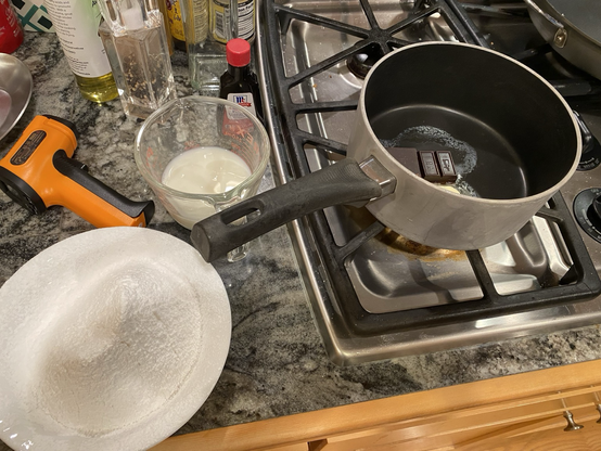 several ingredients next to a pot with melting butter and choco in. also a laser thermometer.