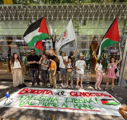 Gli attivisti di fronte al Mc Donald della stazione centrale di Napoli.

9 attivisti con due bandiere della Palestina e una del gruppo "Humanity in Focus". A terra uno striscione, fermato a terra da un megafono e una borsa. Sopra la scritta: "Boicotta il genocidio. Palestina Libera dal fiume al Mare"