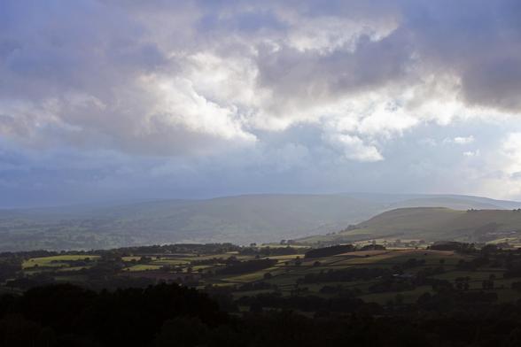 A view towards the end of the Wye Valley with rain clouds over the hills, sunlight breaking through in swathes illuminating the the rolling green pastures below. Wales, UK. 14th June, 2025.