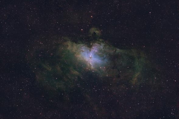 A field of stars with a cloud of multicolored gas that has a resemblance to a large bird of prey striking at some prey