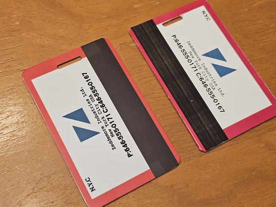 Photo of the reverse side of two Ghostbusters: Frozen Empire engineer badge replicas, with a glossy aluminum badge on the left, and a lower-quality plastic badge with vinyl label on the right.