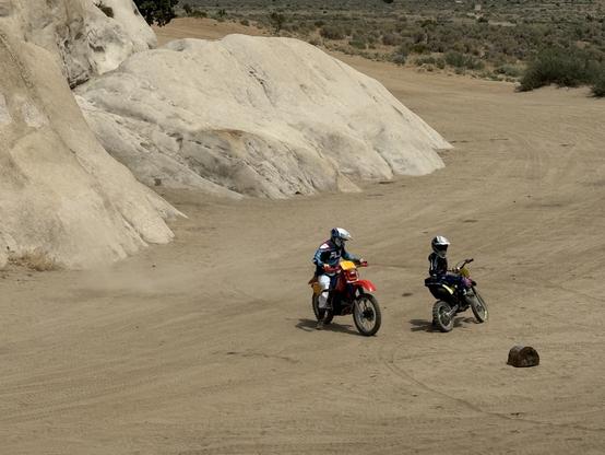 A father and a young son in a full offroad bike gear, with appropriately sized Honda motorcycles. The boy is getting the bike up, and dad is calmly watching, instructing.