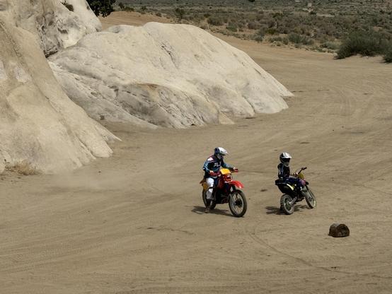 A father and a young son in a full offroad bike gear, with appropriately sized Honda motorcycles. The boy is getting the bike up, and dad is calmly watching, instructing.