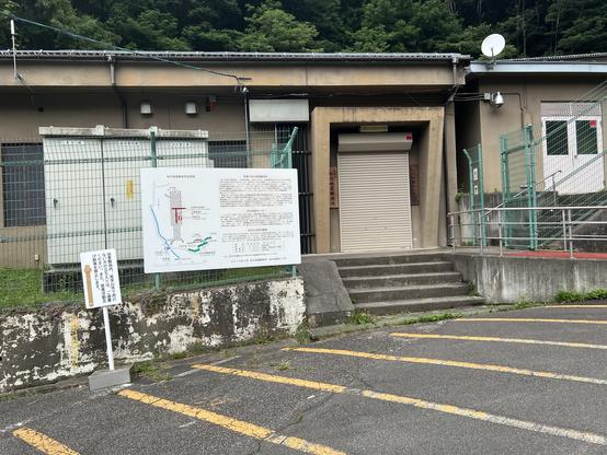 Shuttered entrance of buildings with sign about tunnels under mountain in back of them.