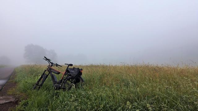 Ein Fahrrad steht im Freien  auf einer Wiese, umgeben von  Nebel.