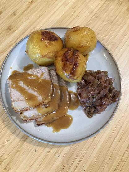 Slices of roast pork with crackling, gravy, caramelized potatoes, cabbage.