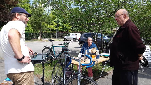 Trois membres de l'asso échangent pendant l'atelier. Un vélo est posé contre la table de l'atelier, un autre à l'arrière-plan est maintenu sur un mini-pied.