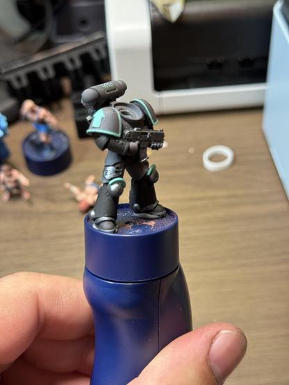 The body of a space marine on a painting handle. It is gray with gunmetal highlights on parts of its armor. The the shoulder rims and emblems are painted turquoise to resemble the classic Hatsune Miku color scheme.