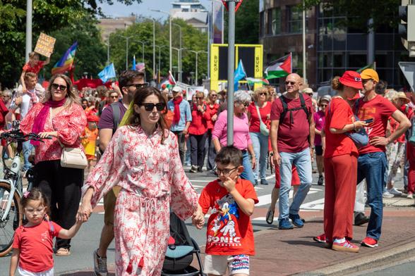 The protesters walk around the corner towards the Peace Palace. In the front left a mother with two children, all three wearing something red. Behind them a large group of protesters.