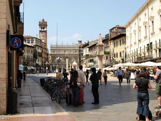 Farbfoto, aufgenommen auf der Piazza delle Erbe in Verona, Veneto, Italien. Der große Platz ist umgeben von historischen Gebäude und bevölkert von zahlreichen Passanten.