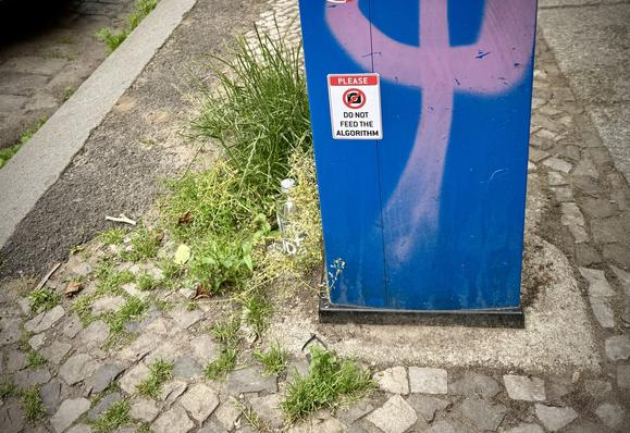 Ein blauer Kasten am Rand des Gehwegs mit einem Sticker „Please do not feed the algorithm“