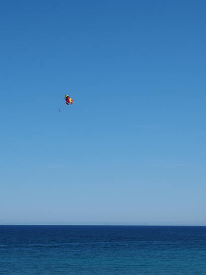 Paraglider mit buntem Gleitschirm im blauem Himmel über dem dunkelblauen Meer.