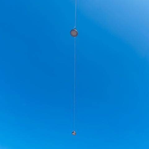 Two circular light fixtures hang from a thin wire against a bright blue sky.