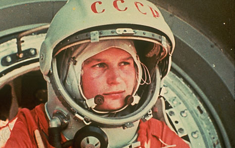 Valentina Tereshkova in her orange spacesuit. She is a white woman wearing a white helmet with CCCP on it.