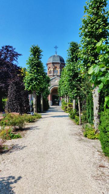 Shell pathway lined by trees, in the distance a cupola with a gateway to the next section.