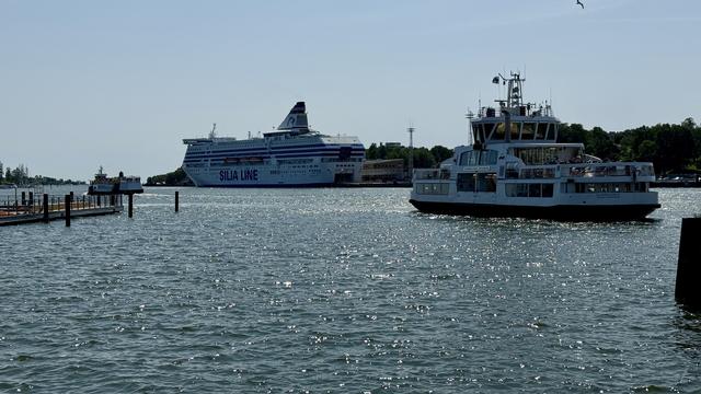 A large cruise ship labeled "Silja Line" is docked in the background, while a smaller ferry is operating in the foreground on sparkling waters. The scene is set under a clear blue sky.