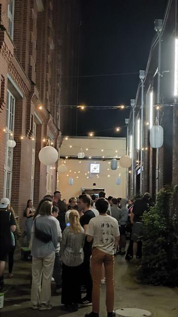 Dekorierte Gasse zwischen alten Backsteingebäuden. Nachts. In der Gasse stehen viele junge Menschen.