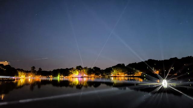 Nächtlicher Blick auf einen See, in dem sich bunte und silberner Lichter spiegeln.