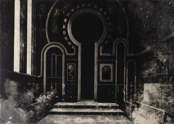 A dimly lit, monochromatic architectural space is depicted in the image. At the center is a large, monumental doorway shaped like an oversized keyhole. The doorway is flanked on either side by symmetrical archways and tall, narrow vertical recesses. The surrounding wall is detailed with ornate framing lines and inset panels, giving a sense of depth and decoration. Two framed motifs resembling abstract medallions or relics are present on each side of the central doorway.

The steps leading up to the entrance are worn and shadowed, creating a dramatic contrast between light and dark areas. The texture throughout the scene is rich, with visible grain and smudging that suggest the surface has been etched, rubbed, or printed. Soft, cloud-like patches spread across the bottom and sides of the composition, adding a slightly mysterious, aged atmosphere.

Overall, the space feels sacred or ceremonial, evoking a timeless, almost religious stillness.