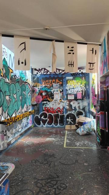 The entrance to CCCZH, covered in beautiful graffiti too complex to describe, with kanji-like characters drawn with black ink on white cloth hanging from a string across the foreground