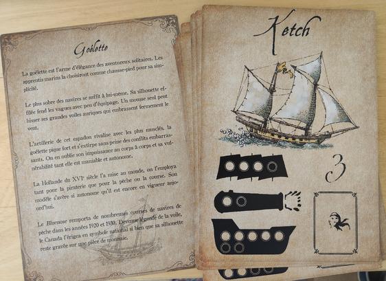 Deux grandes cartes de jeux style parchemin avec une Illustration de ketch (une sorte de navire) et des points associés, et la description d'une goélette : elle est l'arme d'élégance des aventureux solitaires. Les apprentis marins la choisiront comme chausse pieds pour sa simplicité. Le plus sobre des navires se suffit à lui-même. Sa silhouette effilée fend les vagues avec peu d'équipage. Un mousse seul peut hisser ses grandes voiles auriques qui embrassent fermement le vent. L'artillerie de cet espadon rivalise avec les plus musclés, la goélette pusue fort et s'extirpe sans peine des conflits embarrassants. On en oublie son impuissance au corps à corps et sa vulnérabilité tant elle est maniable et autonome. La Hollande du 16eme siècle l'a mise au monde. On l'employa tant pour la piraterie que pour la pêche ou la course. Son modèle s'avère si autonome qu'il est encore en vigueur aujourd'hui. Le bluenoise remporta de nombreuses courses de navires de pêche dans les années 1920 et 30. Devenue légende de la voile, le Canada l'érigea en symbole national, si bien que sa silhouette reste gravée sur une pièce de monnaie.