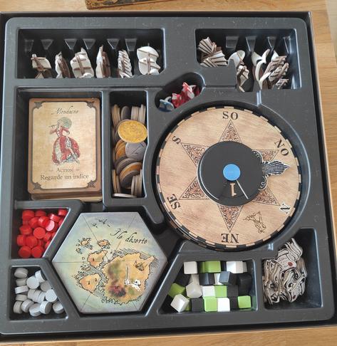 Intérieur de la boite avec des cartes de jeux des boussole, des cartes archipels, des pièces, des jetons, et des navires miniatures.