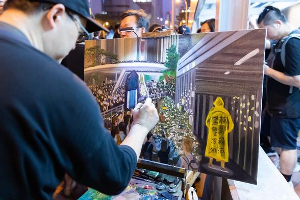 A man painting a painting of Marco Leung who tragically died after falling from scaffolding the evening before this huge protest and the protesters marching through the streets.