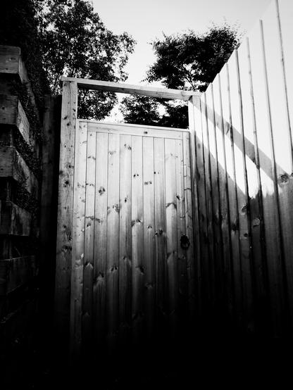 A high wood gate down an alley that is half lit in shadow.