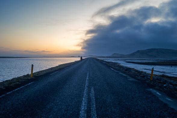 A picture of a road with water on both sides. Sarah walking on the road.