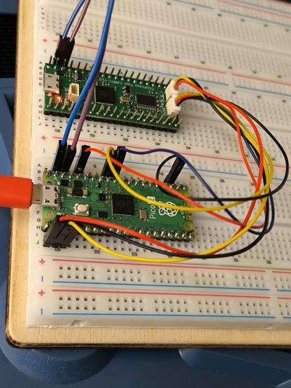 A Raspberry Pi Pico 2 and custom board PCB of the same size. Both are plugged into a white breadboard with wires between the boards.