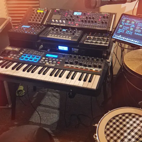 Photo of a keyboard with some synthesizers, an iPad and drums ready set up to be played.