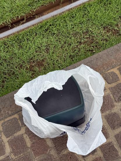 A SiliconGraphics O2 in a thin HARD OFF plastic bag stood next to tram tracks with some smattering of rain on it