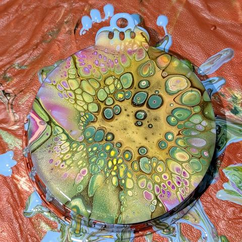 A fluid art bloom on a flat circular holiday ornament. The color palette is a continuation of my cactus flower inspired palette: pinks, yellows, and greens with brown and gold cell activator over a pale blue base. The latter isn't especially visible in this particular piece.