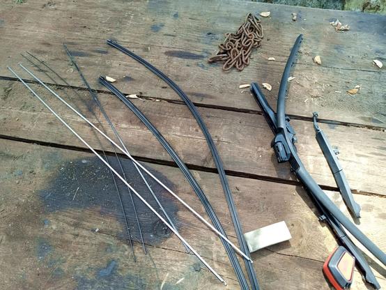 Two windshield wapers taken apart on a grimy workbench. There's steel strips on the left, the rubber profiles in the middle and a pile of plastic parts on the right.